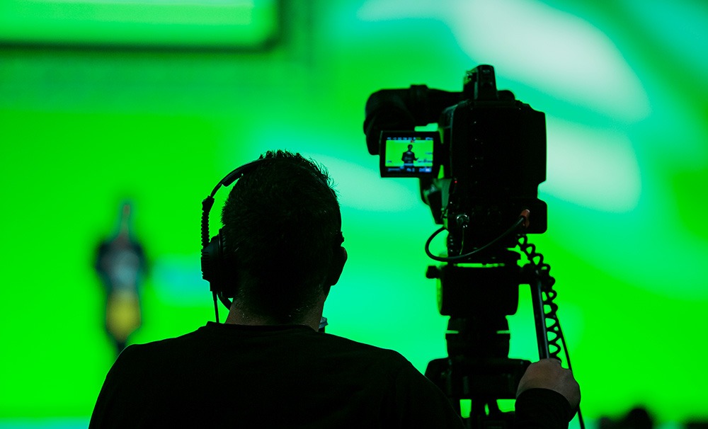Image of a camera operator filming a person in front of a green screen. 